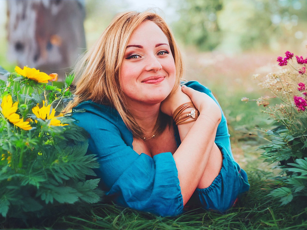 Harmony Vellekamp, owner of Papernpulse and eclectiq media designer, smiling while lying on grass in an outdoor setting.